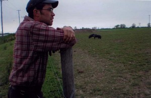 Farmer Gerhard Taves standing by fence. Two pigs are nearby.